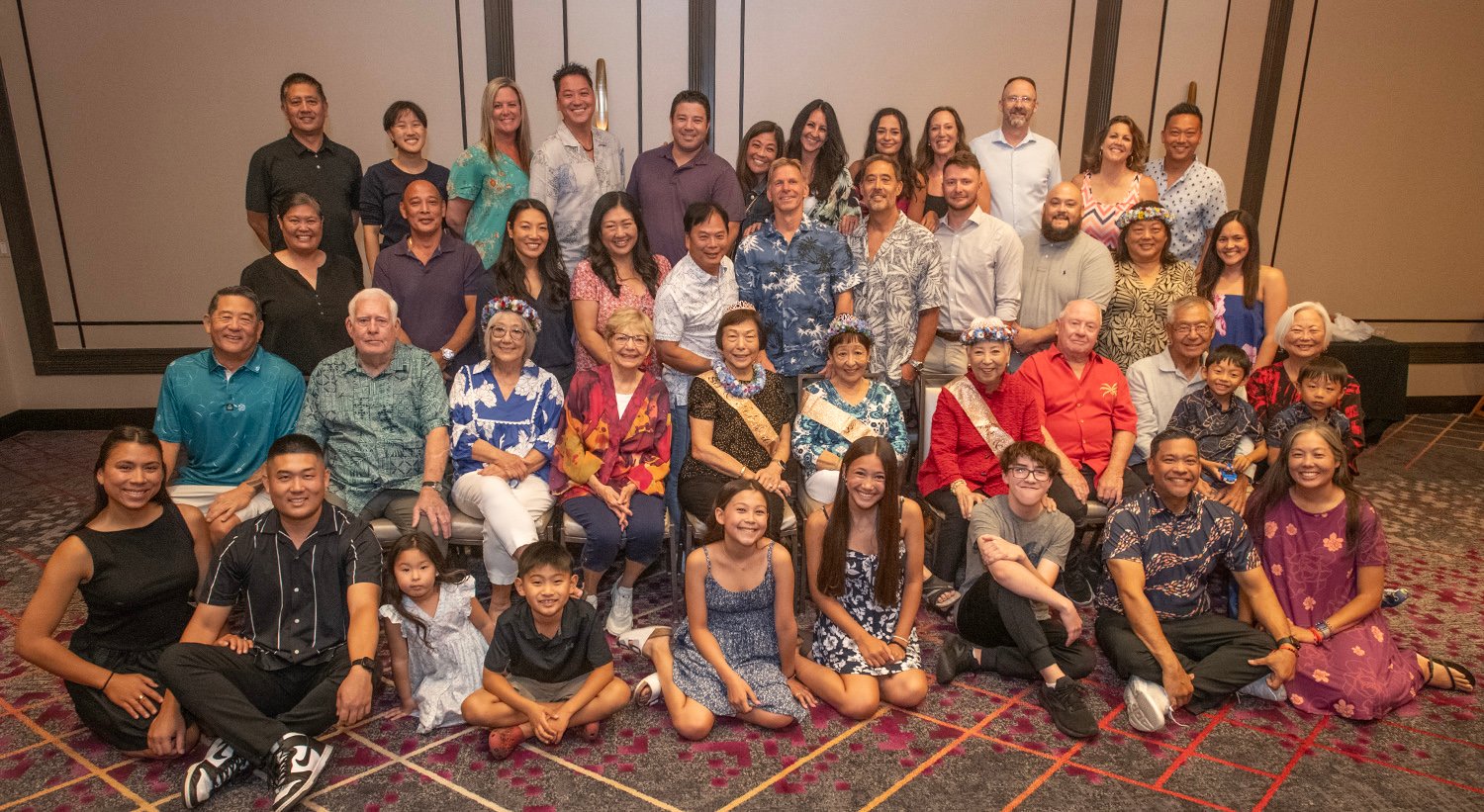 Large group photo at a family reunion in a hotel ballroom; attendees in tropical attire and leis.