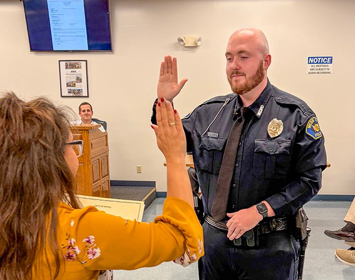 Police officer in uniform high-fives a woman in a mustard blouse during a community event in a courtroom-like room.
