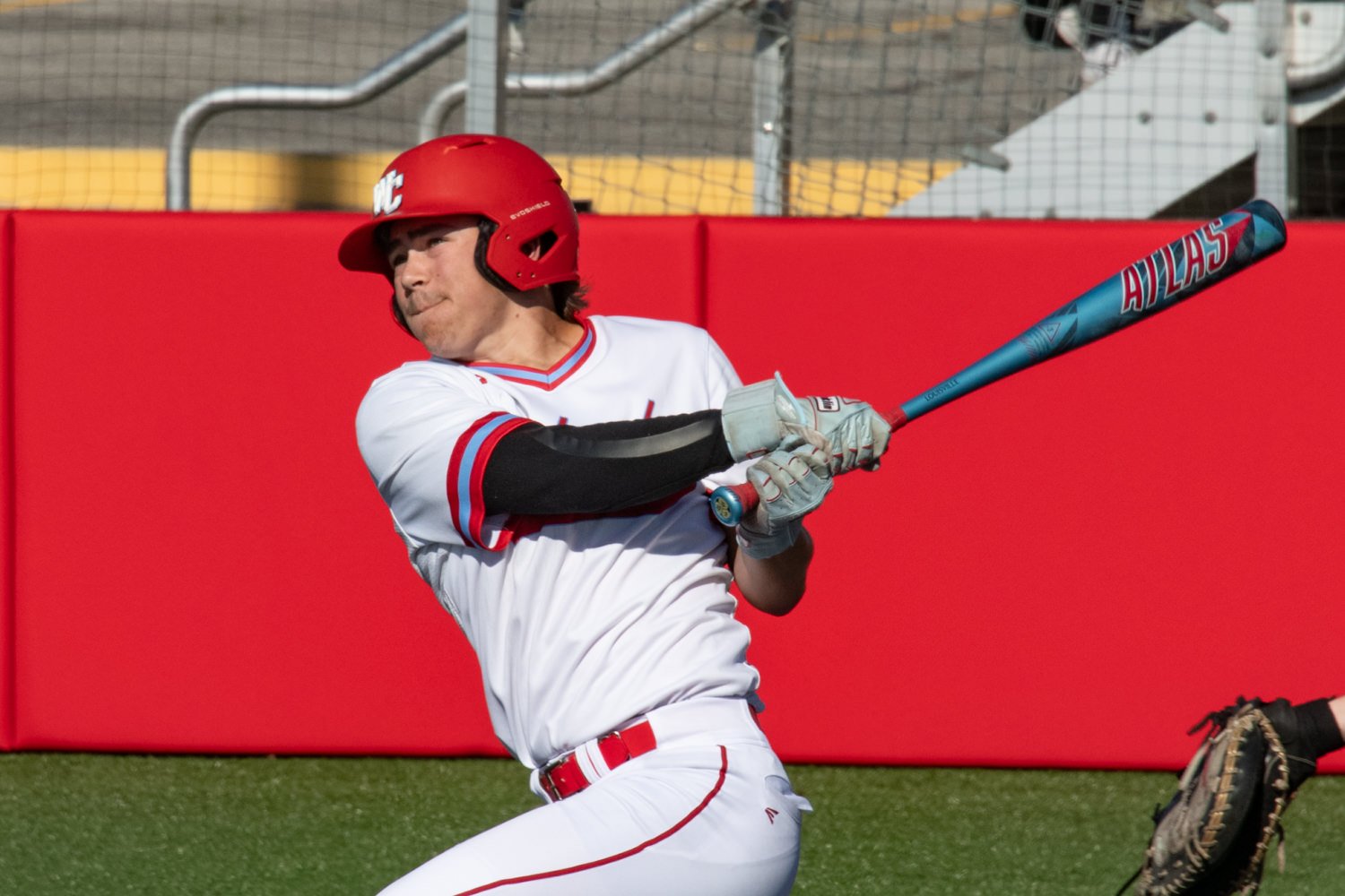 Baseball player in white and red uniform swings a blue Atlas bat during a game on a green field