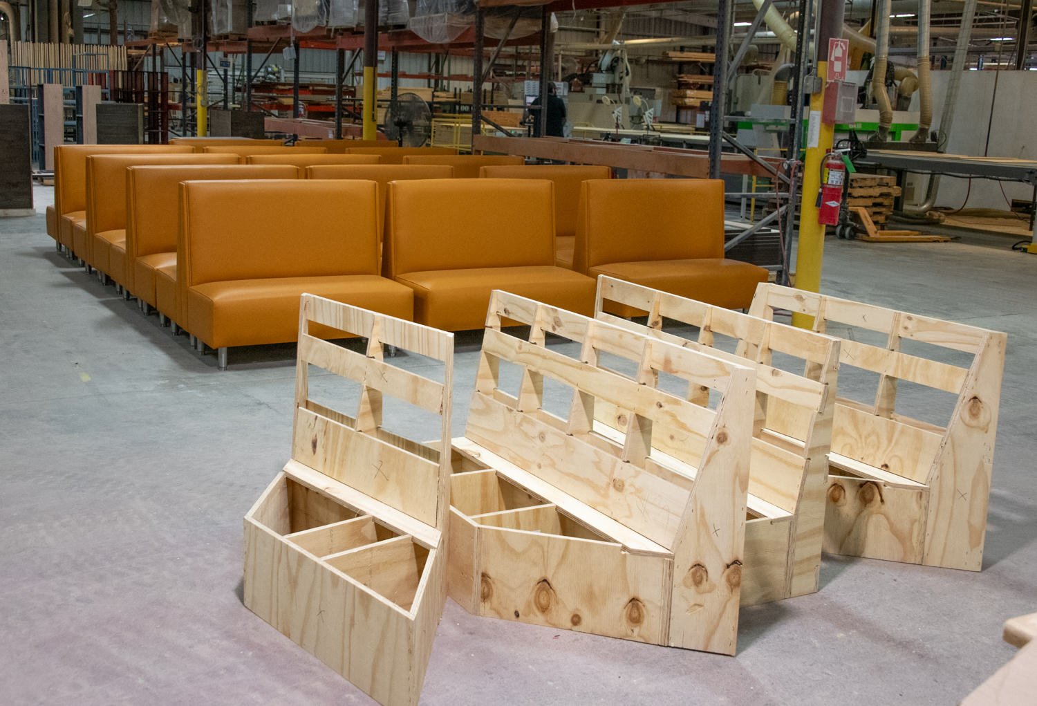 Row of orange modular couches in a factory, with unfinished wooden frames in the foreground.