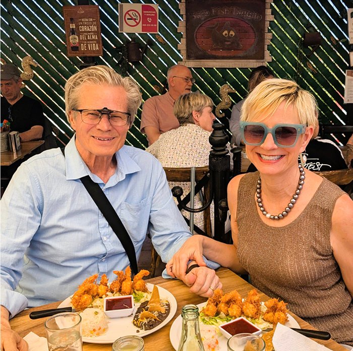Smiling older couple seated at a restaurant table, holding hands over plates of fried appetizers and dipping sauces in front of them.