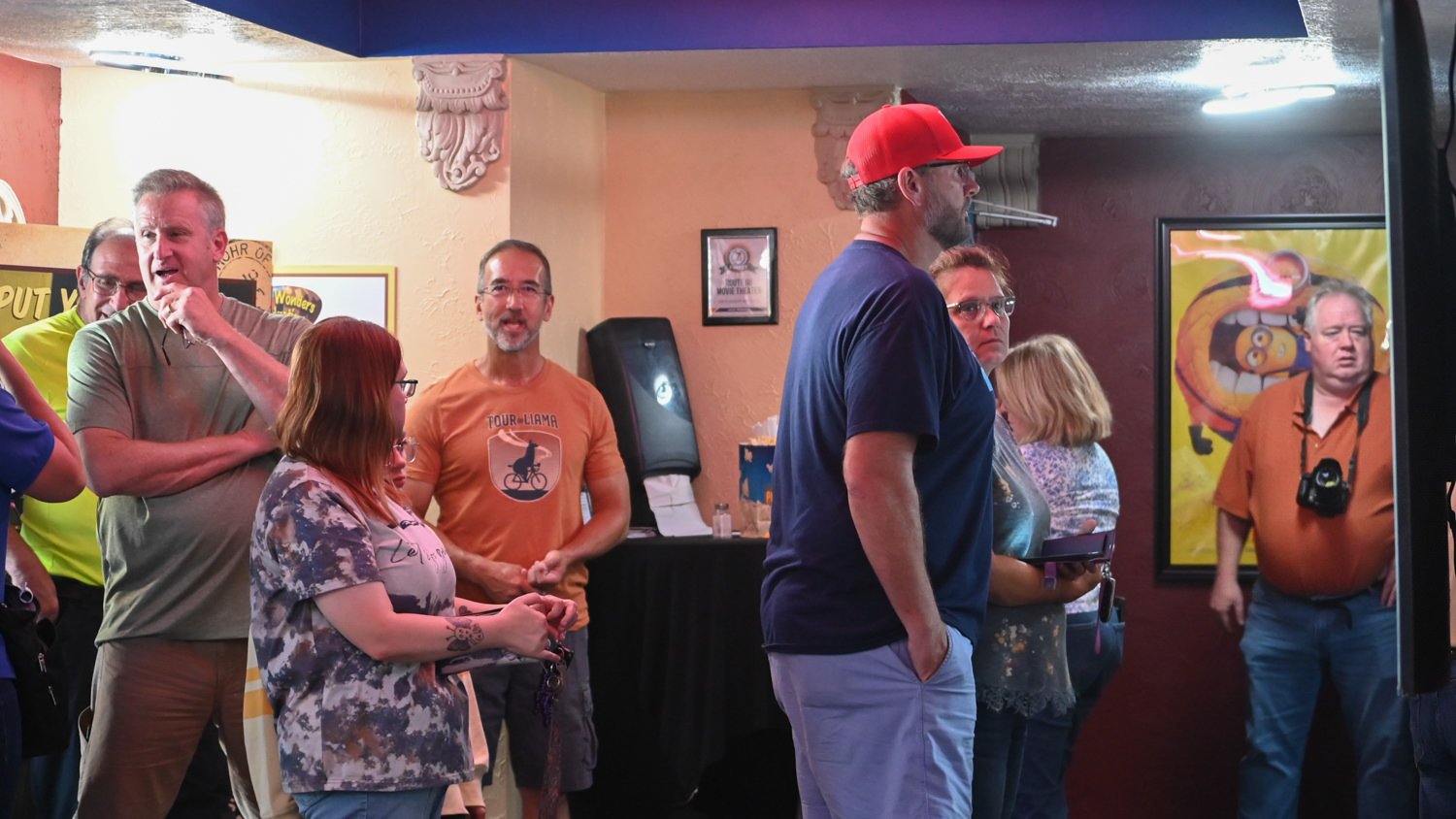 Small group of adults gathered in a cozy, decorated room watching a screen on the right side of the frame.
