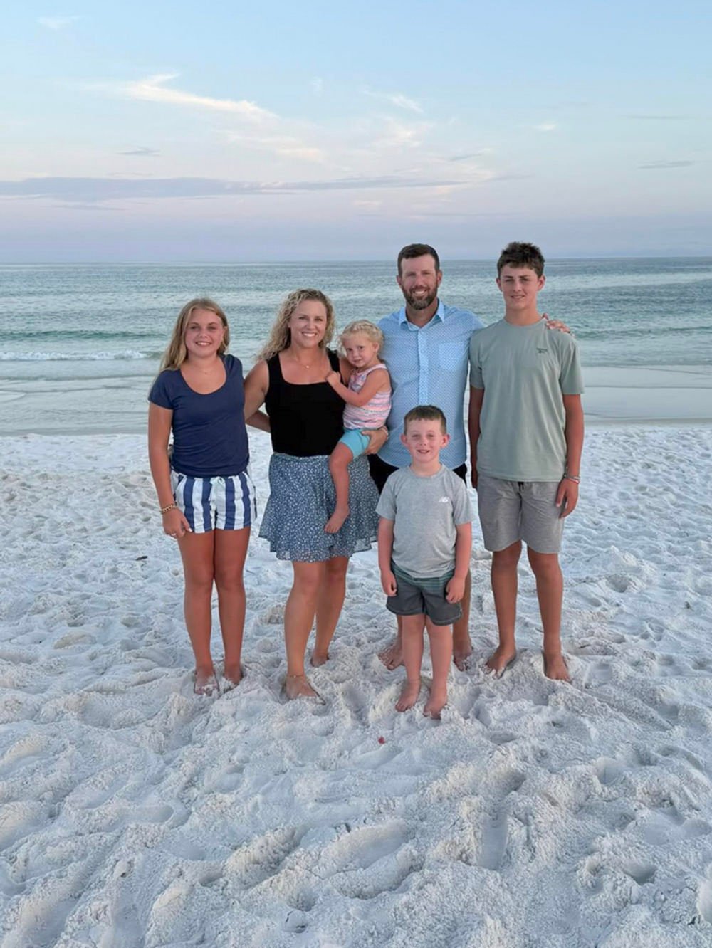 Family of six posing on a white-sand beach with the ocean in the background, smiling at the camera.