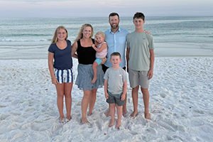 Family of six posing on a sandy beach with the ocean in the background.