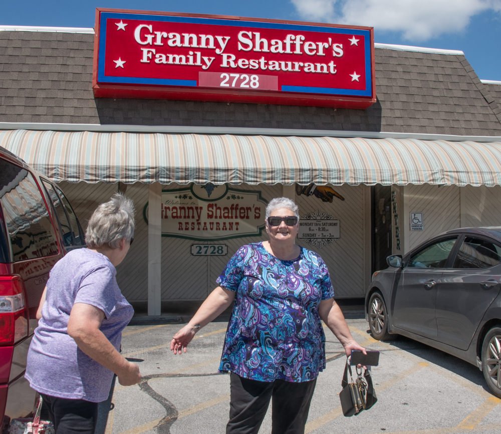 Front view of Granny Shaffer's Family Restaurant storefront with a bright red sign; two women stand in the parking lot outside the entrance.