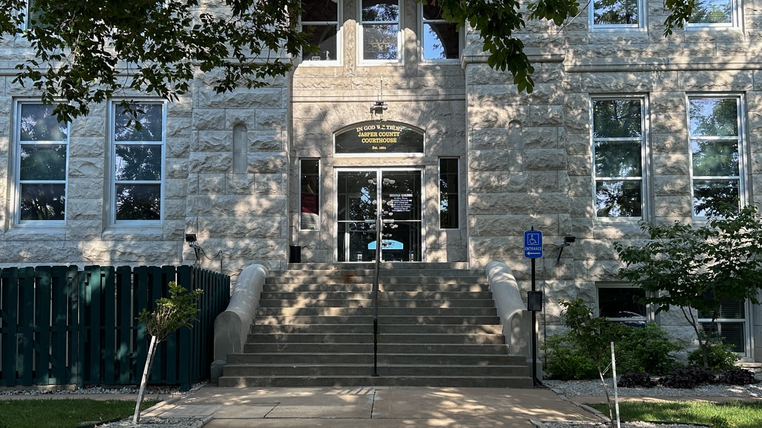Stone courthouse entrance with wide concrete steps and glass doors, flanked by windows and a blue accessibility sign nearby