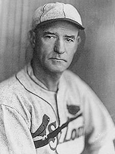 Black-and-white portrait of a mid-20th-century baseball player in a vintage uniform and cap, looking at the camera.