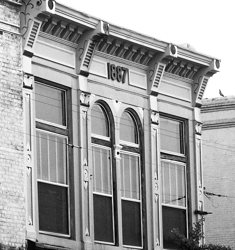 Historic brick storefront with decorative cornice and the year 1887 above arched windows