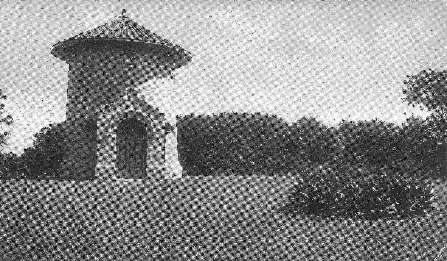 Round tower with a conical tiled roof and ornate arched doorway in a grassy park setting menagerie