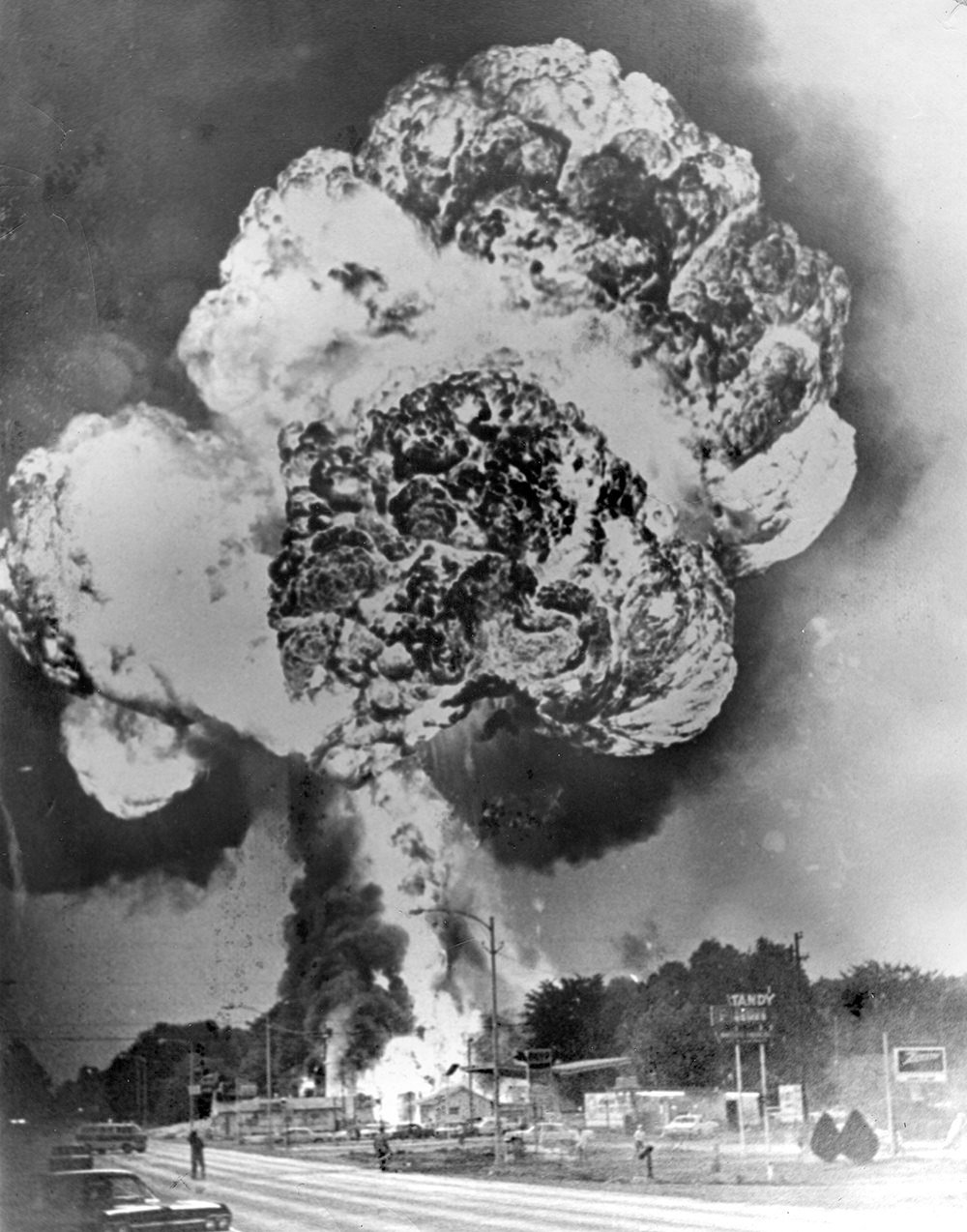 Nuclear explosion with a towering mushroom cloud above a town, smoke columns rising over a street with cars and buildings below