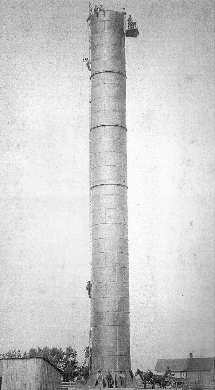 Tall cylindrical tower with people climbing ropes near the top and a platform; workers and a horse-drawn cart at the base.