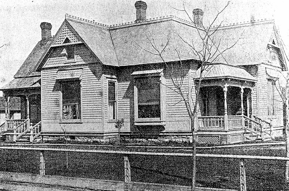 Old two-story wooden house with wraparound porch, bay windows, and a steep gabled roof; bare trees in front.