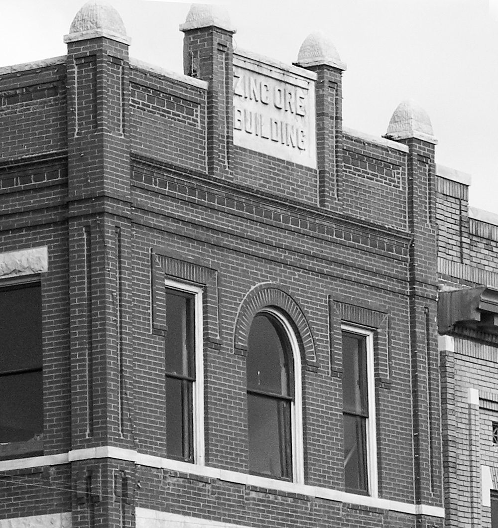 Brick two-story building with arched windows and decorative roofline, featuring a stone plaque with illegible text on the cornice.