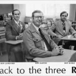 Three men in a classroom sit at old desks, smiling for the camera, with a 'Back to the three R's' caption below.