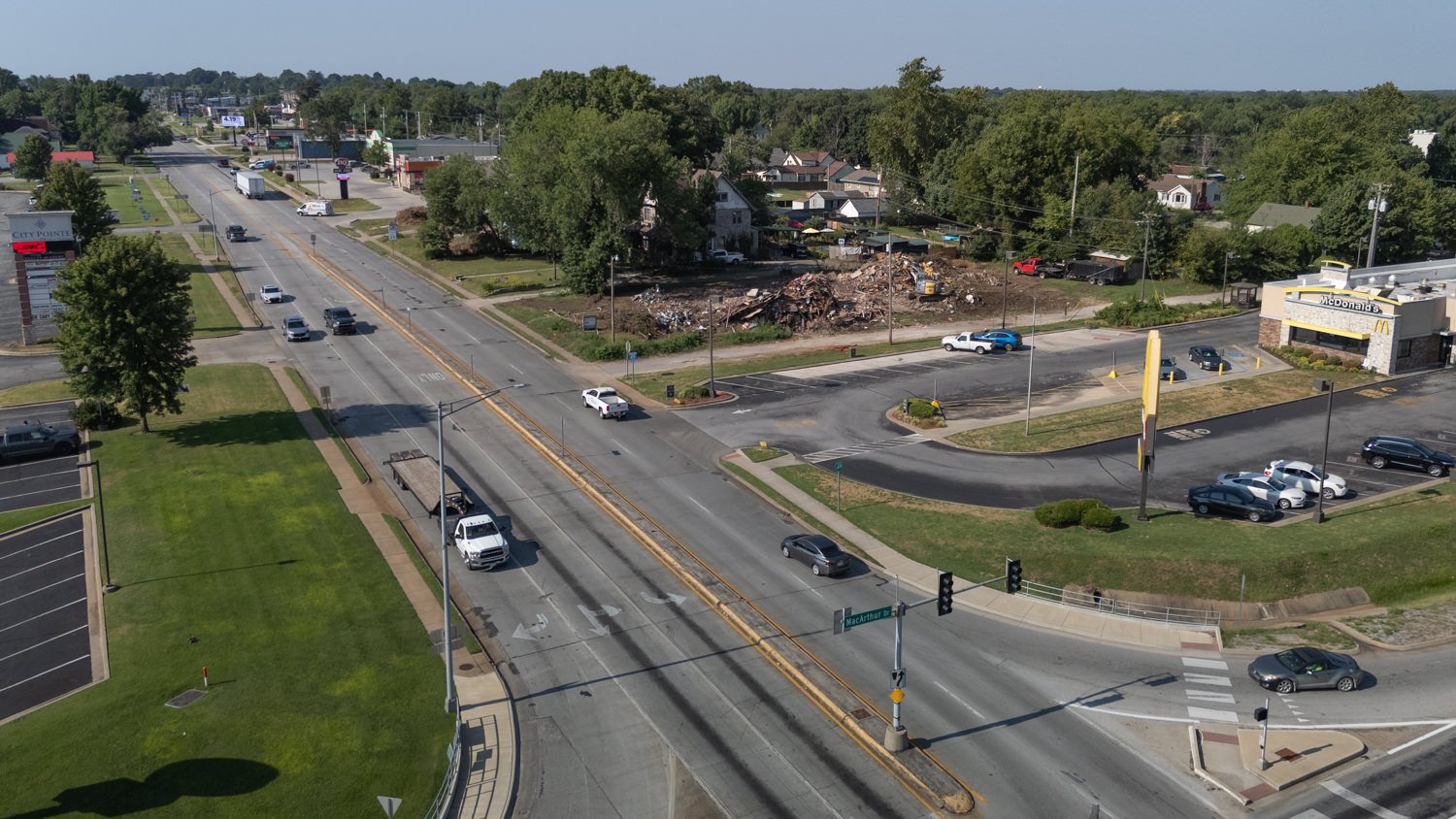 Aerial view of a busy intersection with a large debris pile and a McDonald's on the right; several cars travel the road above a grassy median area.