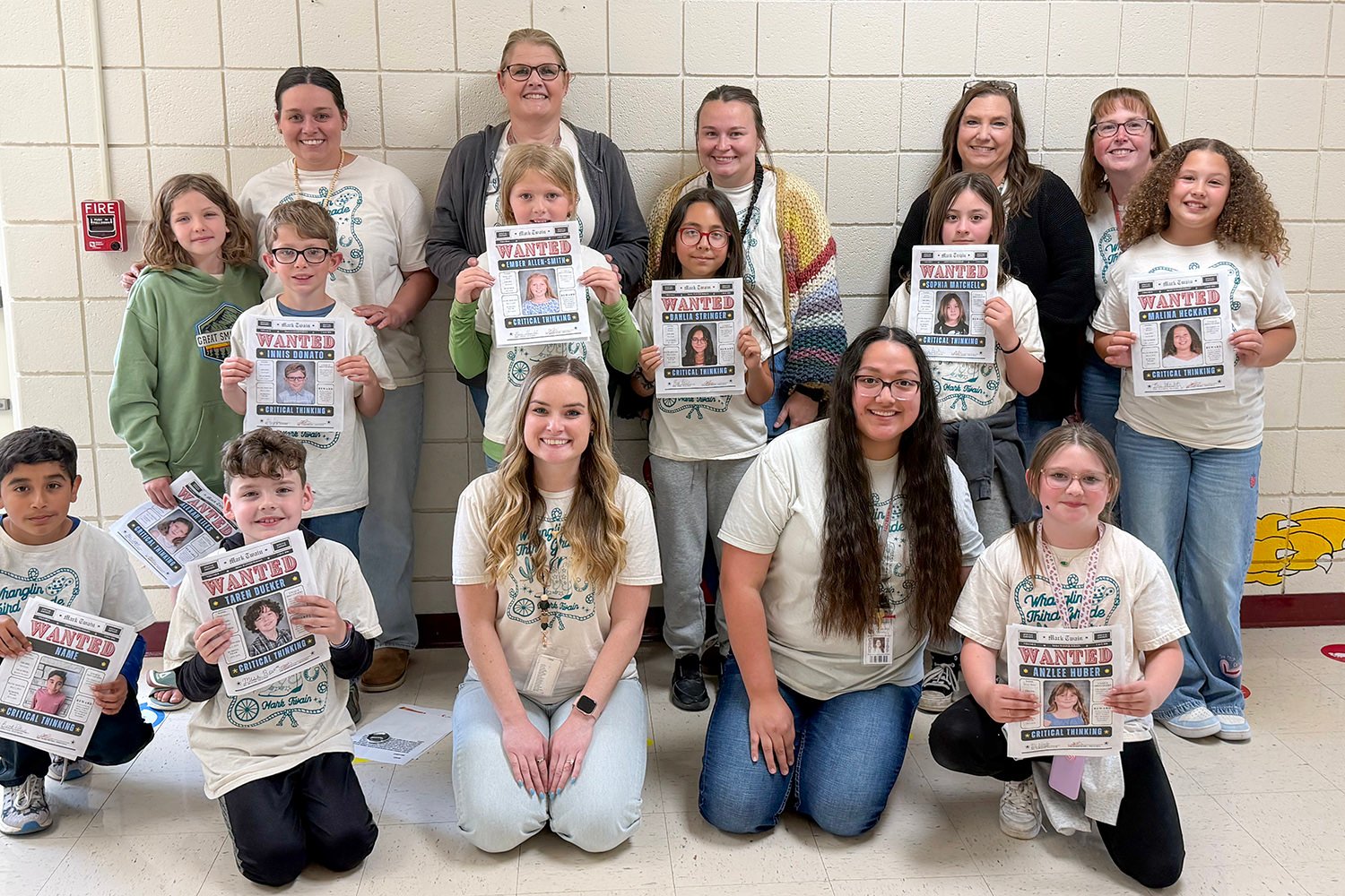 Group of students and teachers stand against a wall, each holding a 'WANTED' poster promoting critical thinking.