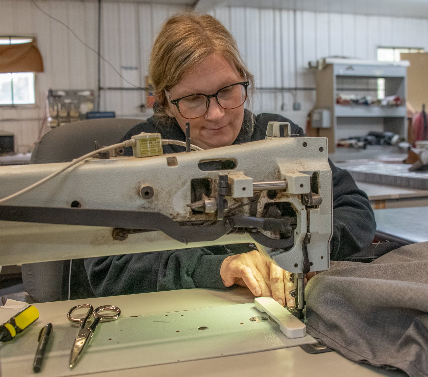 Woman with glasses guiding fabric through an industrial sewing machine in a workshop beneﬁt of a quiet focus hands-on sewing scene.