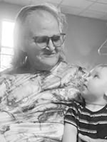 Older man with long hair and sunglasses smiling at a young child in a striped shirt.