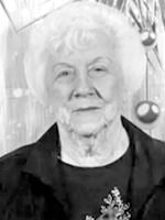 Elderly woman with short white hair and a gentle smile, wearing a dark jacket and a decorative top, indoors near hanging ornaments.
