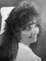Black-and-white head-and-shoulder portrait of a woman with curly hair, smiling over her shoulder.