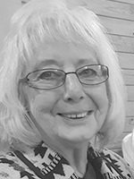Older woman with short light hair and glasses smiling at the camera.