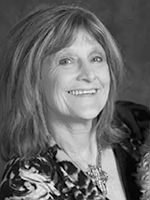 Black-and-white portrait of a smiling woman with shoulder-length hair wearing a patterned blouse.