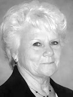 Black-and-white portrait of an older woman with short white hair, wearing a dark blazer and pearl earrings, looking at the camera.