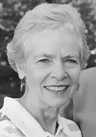 Black-and-white portrait of an elderly woman smiling, with short white hair and a light blouse outwardly looking at the camera.