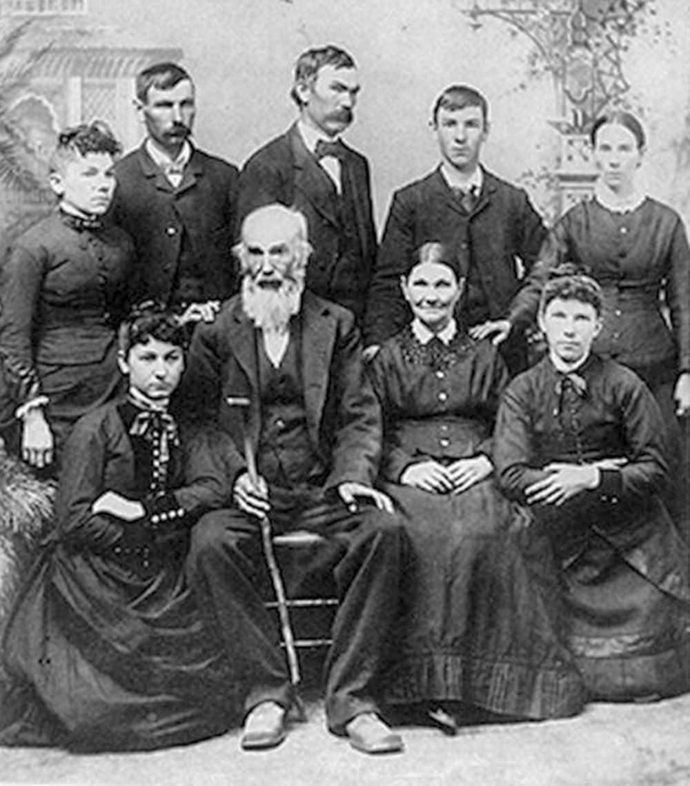 Group portrait of a Victorian-era family: elderly man with a cane seated center, others in formal dress gathered around him (standing and seated).