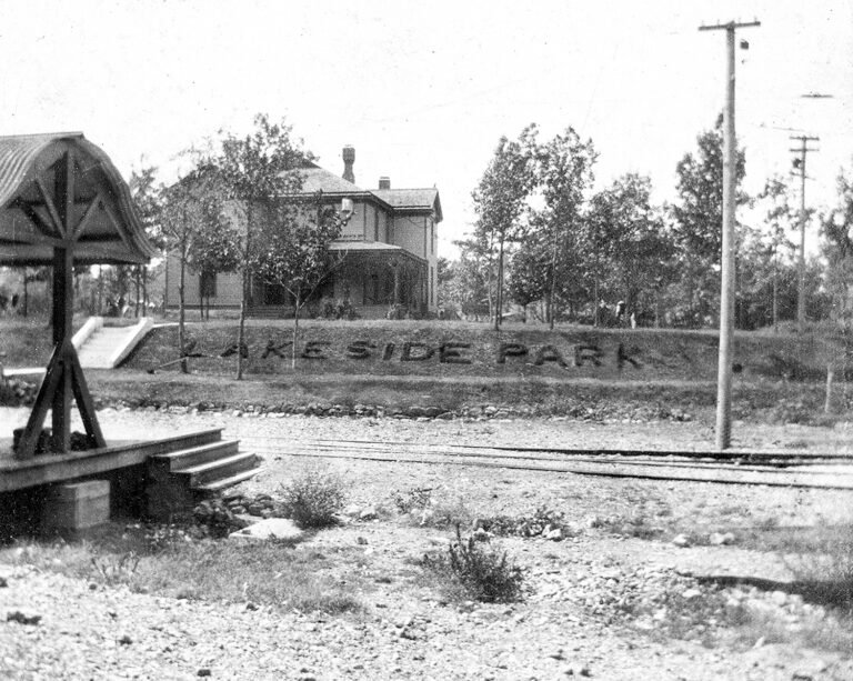 Old railway platform with a shelter on the left and a house beyond; 'KESIDE PARK' letters carved into the grassy slope by the tracks.