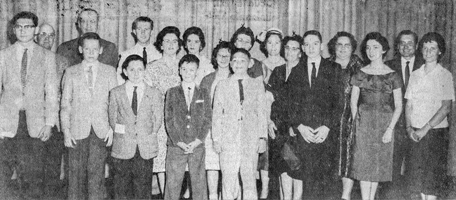 Group of men and women in formal attire posing for a group portrait at a social event (1960s style).