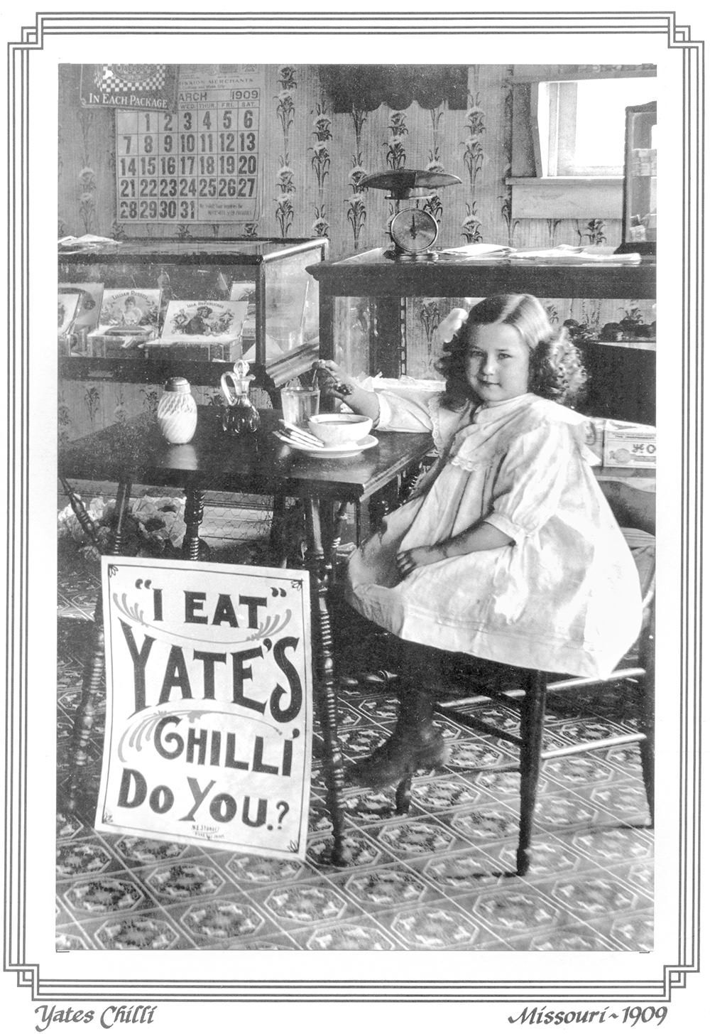 Young girl in a white dress sits at a cafe table beside a large sign reading 'I EAT YATES CHILLI DO YOU?' (Missouri, 1909).