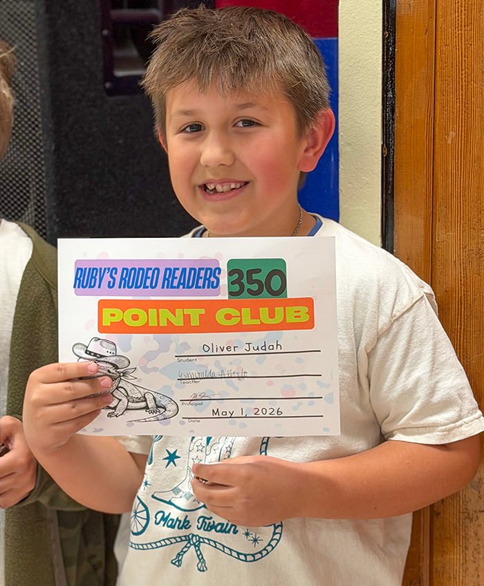 Boy smiles while holding a 'Point Club' certificate for Ruby's Rodeo Readers, name Oliver Judah, dated May 1, 2026.