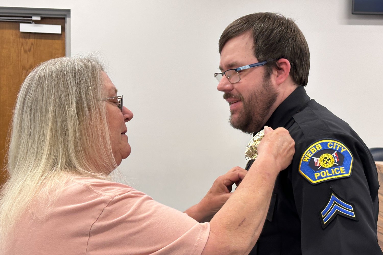 Older woman with gray hair pins a gold medal onto a Webb City police officer's uniform during a ceremony.