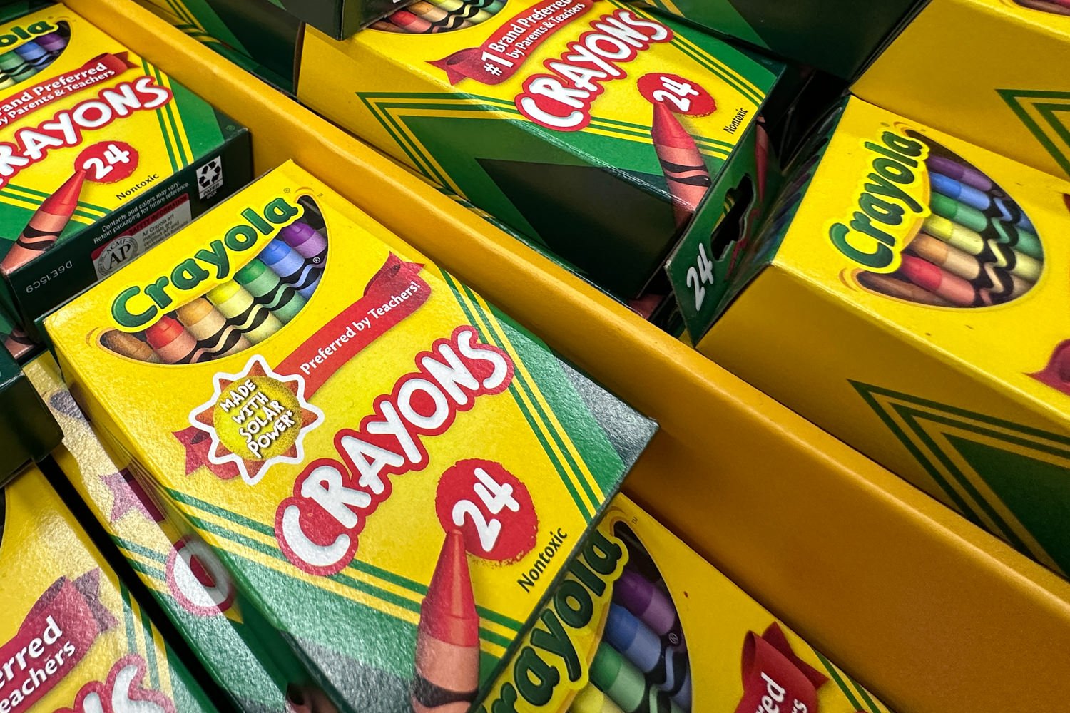 Crayola 24-pack crayon boxes with bright yellow packaging piled together on a shelf.