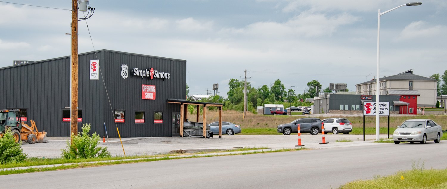 New Simple Simon's pizza restaurant under construction with an orange sign reading OPENING SOON and parked cars nearby.