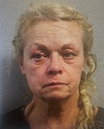 Older woman with light hair in a loose braid, neutral expression, facing the camera against a gray background.