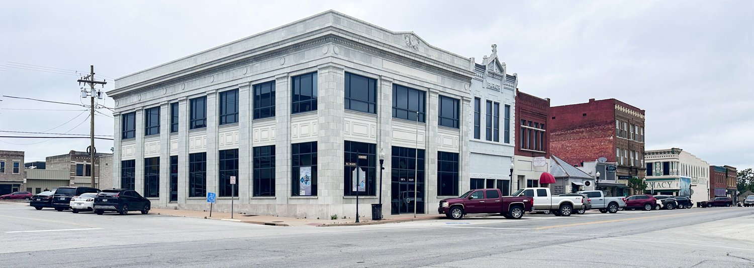 Corner street view with a large white stone corner building and several parked cars along the curb.",